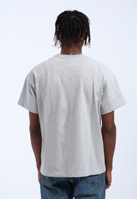 Camiseta de algodón gris con un ajuste relajado y mangas cortas. La parte posterior presenta una textura simple y suave, sin logotipos ni gráficos visibles.
