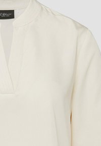 Blouse à manches longues couleur crème avec un col mandarin et un détail d'encolure en V.