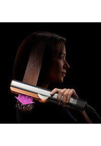 Hårutjämnare med en stilren silverkropp, rosegulddetaljer och ett texturerat grepp, som visar ångapplikation på hår.