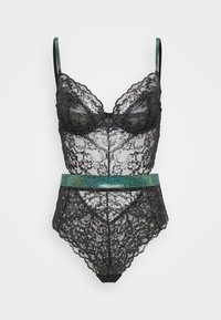 Črn čipkast bodysuit z oblazinjenimi skodelicami, valovitimi robovi in detajlom v pasu z akcentom turkiznih rhinestones. Vključene so nastavljive naramnice.