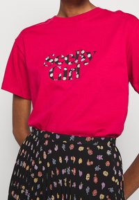 Lyserød bomulds t-shirt med teksten "geeky Girl", prydet med blomsterpatter. Kombineret med en sort plisseret nederdel dekoreret med farverige blomster.