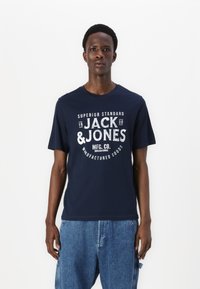 Navy blue short-sleeved t-shirt featuring white text design that includes "JACK & JONES" and other details. Cotton fabric, standard fit.