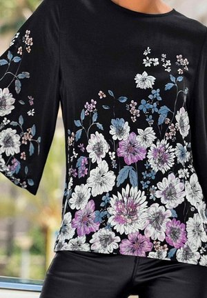 Top negro con estampado floral en blanco, rosa y azul. Tiene mangas anchas y una textura suave, diseñado para un ajuste relajado.