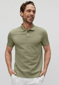 Oliven grøn polo shirt lavet af blødt materiale, med klassisk krave, to-knap placket og minimal branding på brystet.