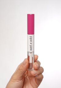 Tubo di lucidalabbra trasparente con cappuccio rosa e corpo bianco, dotato di una sezione trasparente per visualizzare il prodotto, tenuto in una mano.