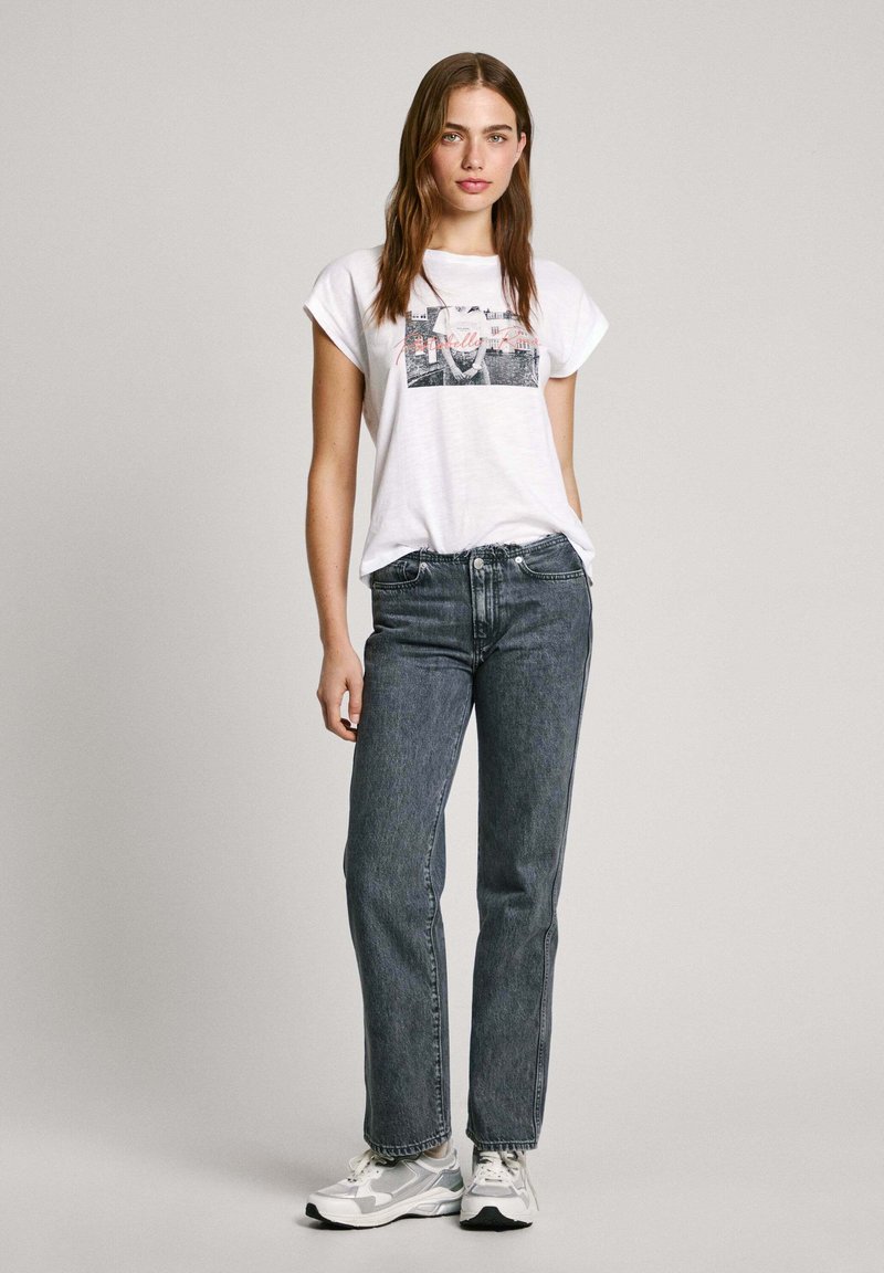 Weißes Baumwoll-T-Shirt mit grafischem Druck, kombiniert mit dunkelblauen Jeans im geraden Schnitt und grauen Sneakern; einfaches Design und lässige Passform.