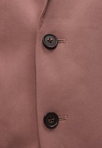 Κοντινή λήψη καφέ υφάσματος με δύο σκούρα στρογγυλά κουμπιά και ραμμένες τρύπες κουμπιών σε ένα ένδυμα.