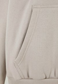 Hoodie beige clair avec une poche kangourou, fabriqué dans un tissu texturé, doté de poignets et d'ourlet côtelés avec des détails de couture visibles.