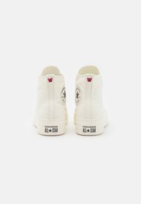 Zapatillas altas de lona blanca con bordados de mariposas rosas, parche del logo de Converse y la marca "ALL STAR" en negro en el talón.
