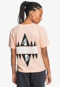 Short-sleeve, light pink cotton t-shirt featuring a large black graphic design with white "Quiksilver" text on the back, triangular accents.