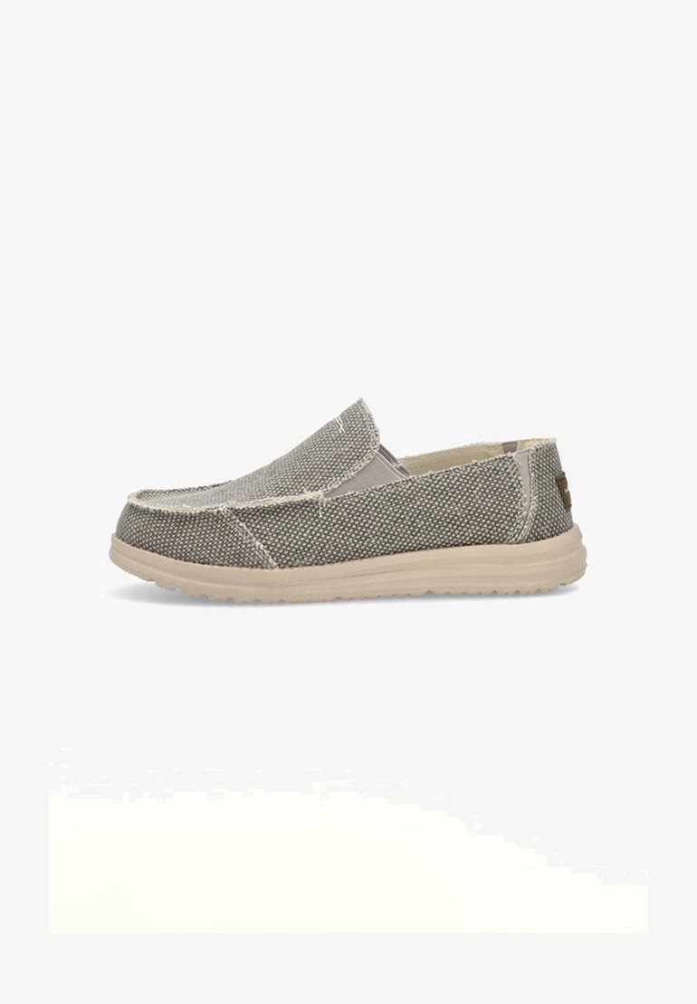Zapato tipo slip-on en tejido gris texturizado con suela de goma beige, con puntera redondeada y costuras visibles a lo largo de las costuras.