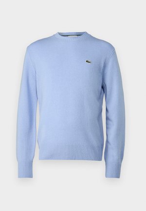 Jasnoniebieski sweter z dzianiny z prążkowanymi wykończeniami na dole i przy rękawach, z małym zielonym logo krokodyla na piersi. Klasyczny fason z okrągłym dekoltem.