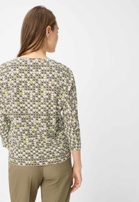 Patroontop met een mix van zigzagontwerpen in olijfgroen, donkerblauw en beige, met driekwart mouwen en een ronde halslijn.