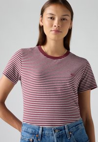 Red and white striped t-shirt with a round neckline and short sleeves. Features a small logo on the left chest. Worn with high-waisted denim.