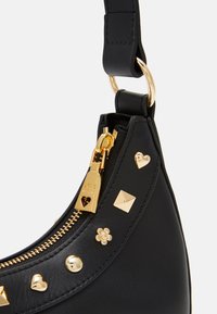 Svart läderhandväska med guldfärgad hårdvara, dragkedjestängning och dekorativa nitar inklusive hjärtan, kvadrater och en blomaccent.