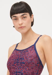 Top da bagno con motivo rosso e blu, dotato di spalline sottili e di un design testurizzato che ricorda la pelle di rettile. Finitura in tessuto liscia.