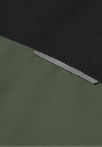 Zbliżenie na warstwy tkaniny w ciemnozielonym i czarnym kolorze, z małym odblaskowym szarym paskiem wszytym pomiędzy nimi.