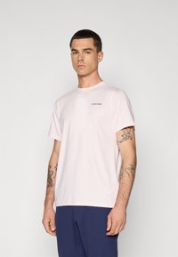 Svetlo roza kratkolisna majica iz mehkega materiala. Ima okroglo ovratnik in majhen temnosiv logotip Calvin Klein na levi strani prsnega koša.