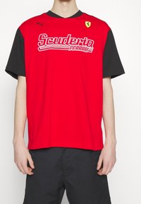 Camiseta de manga corta en rojo y negro con el logo de "Scuderia Ferrari", fabricada en algodón, con cuello redondo y mangas de color contrastante.