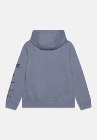 Sweat à capuche gris avec une poche kangourou à l'avant, cordon de serrage à la capuche et texte imprimé en noir le long de la manche gauche. Tissu doux avec une texture lisse.