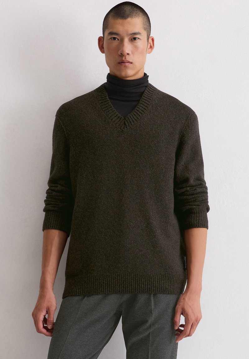 Dunkelgrüner V-Ausschnitt-Pullover aus strukturiertem Strickstoff, mit gerippten Bündchen und Saum. Trägt man über einem schwarzen Rollkragenpullover.