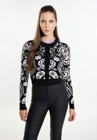 Cardigan a pattern bianco e nero con scollo rotondo, maniche lunghe e bottoni neri; abbinato a pantaloni neri aderenti.