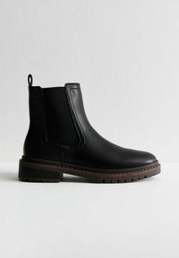 Las botas negras de cuero hasta el tobillo cuentan con paneles laterales elásticos, un lazo en la parte posterior y una suela de goma marrón resistente con surcos poco profundos para mayor tracción.