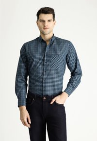 Camicia a quadri verde scuro e blu navy con maniche lunghe, apertura con bottoni, taschino sul petto e tessuto morbido, abbinata a jeans scuri.