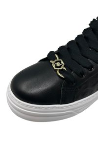 Sneaker in pelle nera con punta rotonda, superficie texturizzata, dettaglio in metallo dorato sui lacci e suola in gomma bianca.