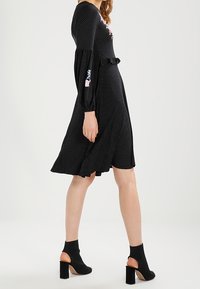 Vestido negro con lunares, de manga larga, con cintura fruncida y bordado floral. Llevado con botas negras hasta el tobillo con detalles recortados.