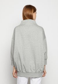 Överdimensionerad grå sweatshirt i mjukt tyg med funnelkrage, nedhasade axlar och elastisk nederkant. Slät textur och avslappnad passform.