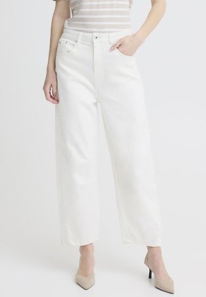 Kvinde iført hvide højtaljede, vidde bukser med forlommer, kombineret med beige spidse hæle og en striped top.