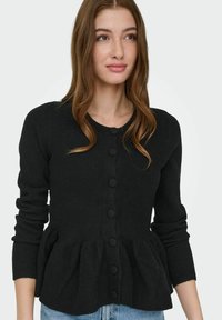 Sort cardigan i en struktureret strik med peplumkant, der har en rundet halsudskæring og knapper foran. Figursyede ærmer, der går til håndleddene.