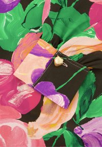 Bloes met bloemenprint in levendige roze, paarse en groene patronen op een zwarte achtergrond. Accent met een gouden aardbei-vormige knoop.