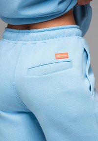 Pantalons de survêtement bleu clair en tissu doux, avec une taille élastique, des poches latérales et une étiquette orange "LEVEL UP".
