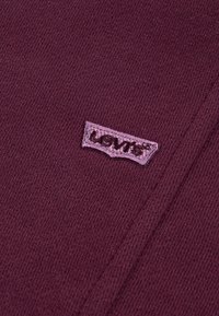 Prim-plan al unei țesături bărmăleu cu o mică etichetă roz Levi's cusută pe suprafață.