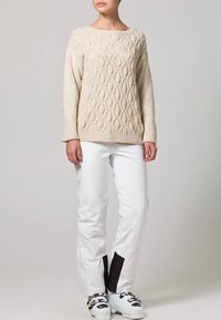 Crèmekleurige kabelgebreide trui met een ronde hals en geribbelde manchetten, gecombineerd met witte broek met zwarte accenten en skistiefels.