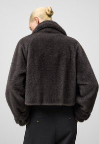 Szara krótka kurtka futrzana o miękkiej, puszystej fakturze, z szerokim kołnierzem i lekko oversize’owymi rękawami, zestawiona z dopasowanymi szarymi spodniami.