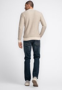 Beige knitted sweater with textured patterns, ribbed cuffs, paired with dark blue jeans and light-colored sneakers.