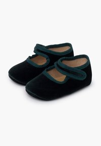 Un par de pequeñas zapatillas de bebé de terciopelo negro con ribete verde y una sola tira en la parte superior sobre un fondo blanco.