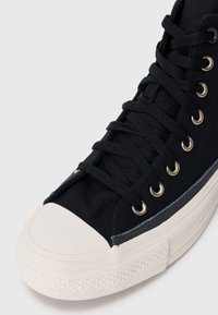 Sneaker nera in tela con punta in gomma bianca, occhielli in metallo e suola testurizzata. Presenta un design con lacci per una vestibilità regolabile.