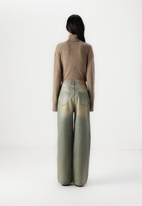 Beige turtleneck genser og vid ben jeans med gradientmønster, som går fra lys grønn til mørkere nyanser ved kanten.