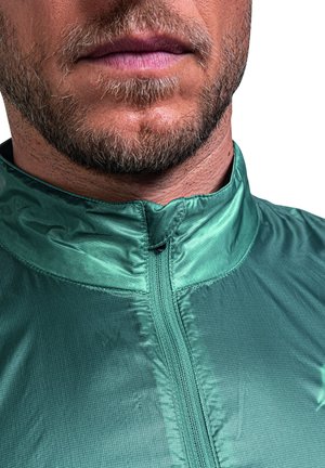 Grüne Jacke mit Reißverschluss und hohem Kragen, strukturierter Stoff und Rautenmuster. Nahaufnahme, die den Reißverschluss und das Kragendesign hervorhebt.