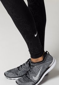 Leggings neri con un motivo testurizzato, abbinati a scarpe da ginnastica grigie e nere con logo swoosh bianco e suola bianca.