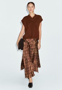 Top sans manches en bronze tricoté avec un col en V, associé à une jupe maxi marron à motifs avec un design en diamant, et des mules noires.