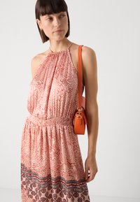 Robe à dos nu en tissu pêche doux avec un motif floral, taille cintrée, et un sac bandoulière orange avec des accents en métal doré.