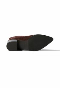 Zapato de tacón alto de ante marrón con punta afilada y suela de goma negra, que presenta un detalle texturizado en el borde superior.