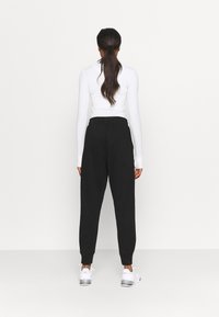 Zwarte sweatpants met een relaxte pasvorm en een elastische tailleband, gecombineerd met een aansluitend wit longsleeve shirt. Gladde stofstructuur, eenvoudig ontwerp.