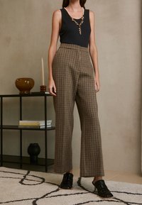 Bruna och svarta rutig högmidjade byxor i kombination med en svart linne, kompletterat med platta, öppna svarta sandaler.