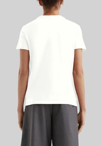 Weißes T-Shirt mit kurzen Ärmeln und rundem Halsausschnitt, glatter Textur, geradem Schnitt und leichtem Seitenschlitz am unteren Saum. Rückansicht wird angezeigt.